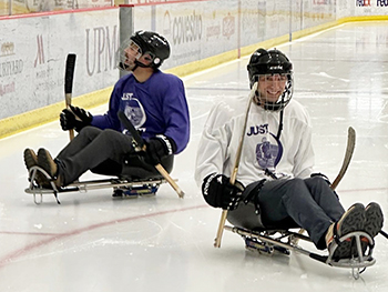 Two individuals playing sled hockey on ice